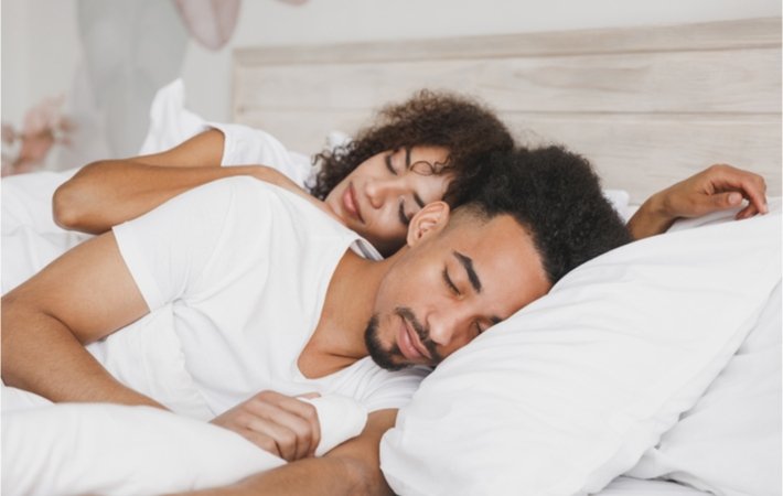 Happy young couple having. a comfortable sleep with the wife leaning up against the husband's back and embracing him.