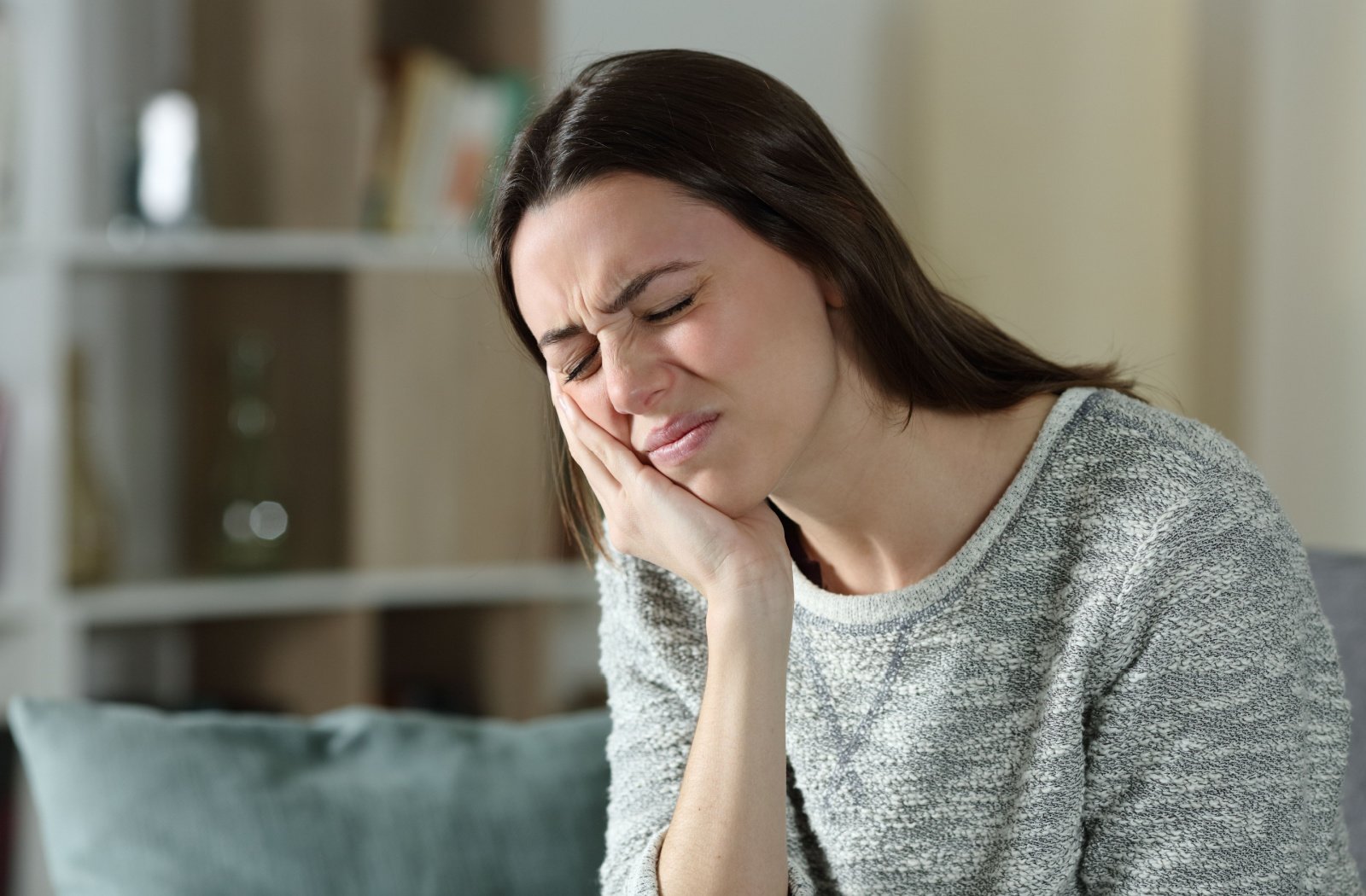 A woman suffering from a toothache holds her right cheek with her right hand.