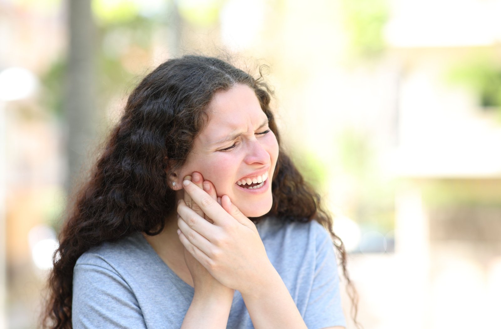 A woman suffering from TMJ holds her left cheek with both her hands.