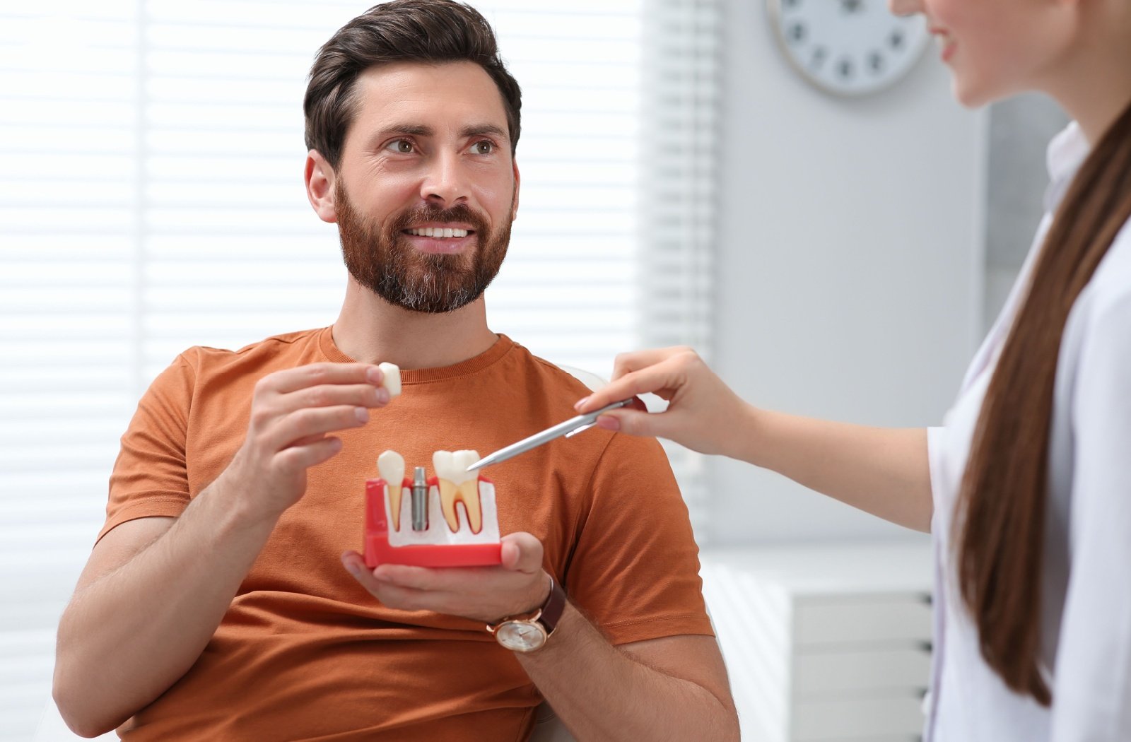 A dentist explaining a dental procedure to a man holding an educational model dental implant