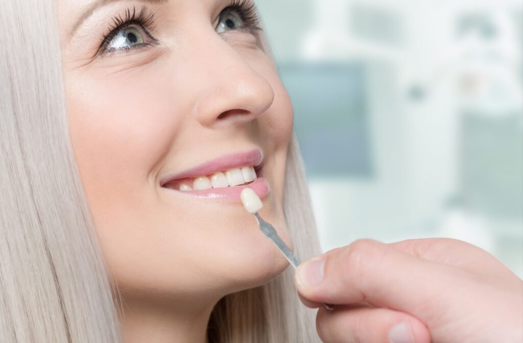 A closeup of a woman's face while a veneer is held up close to her teeth