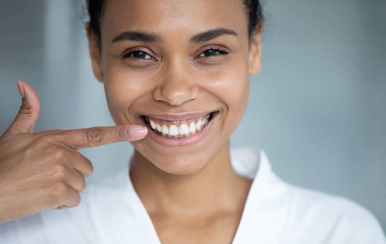 A young person wearing a white shirt smiles confidently and points towards their straight white teeth.