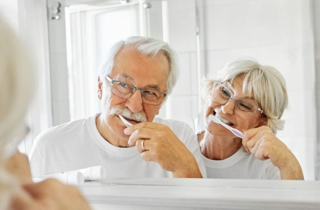 Senior couple brushing their teeth together in front of a bathroom mirror.